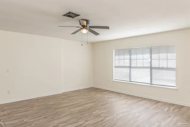 an empty room with wooden floor ceiling fan and windows