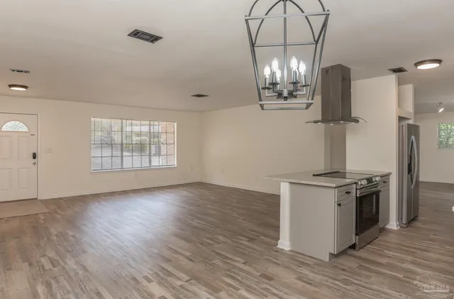 an empty room with wooden floor kitchen view and a chandelier
