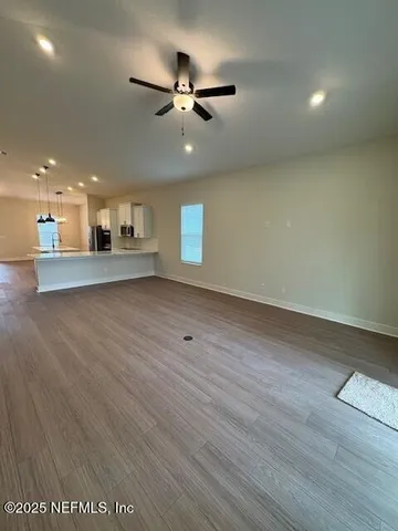 an empty room with wooden floor a ceiling fan and kitchen view