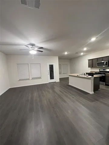 a view of an empty room with wooden floor and kitchen
