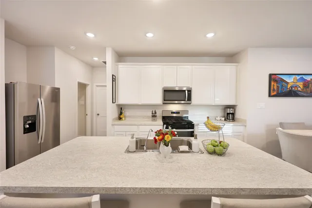 a kitchen with stainless steel appliances kitchen island granite countertop a refrigerator a stove a sink a stove and white cabinets with wooden floor