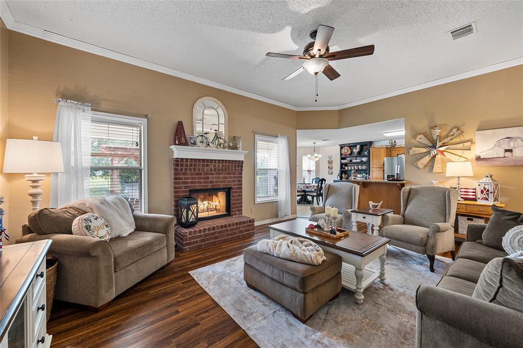 4617 Lexington Street Waco, TX 76705 - Photo 2 of 14 Spacious living area featuring a brick fireplace with mantel, wood-finish flooring, crown molding, and a ceiling fan