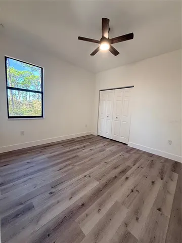 a view of an empty room with wooden floor and a ceiling fan