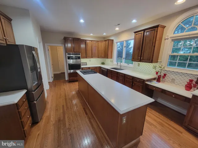 a kitchen with stainless steel appliances granite countertop a refrigerator a sink dishwasher a stove and white countertops with wooden floor