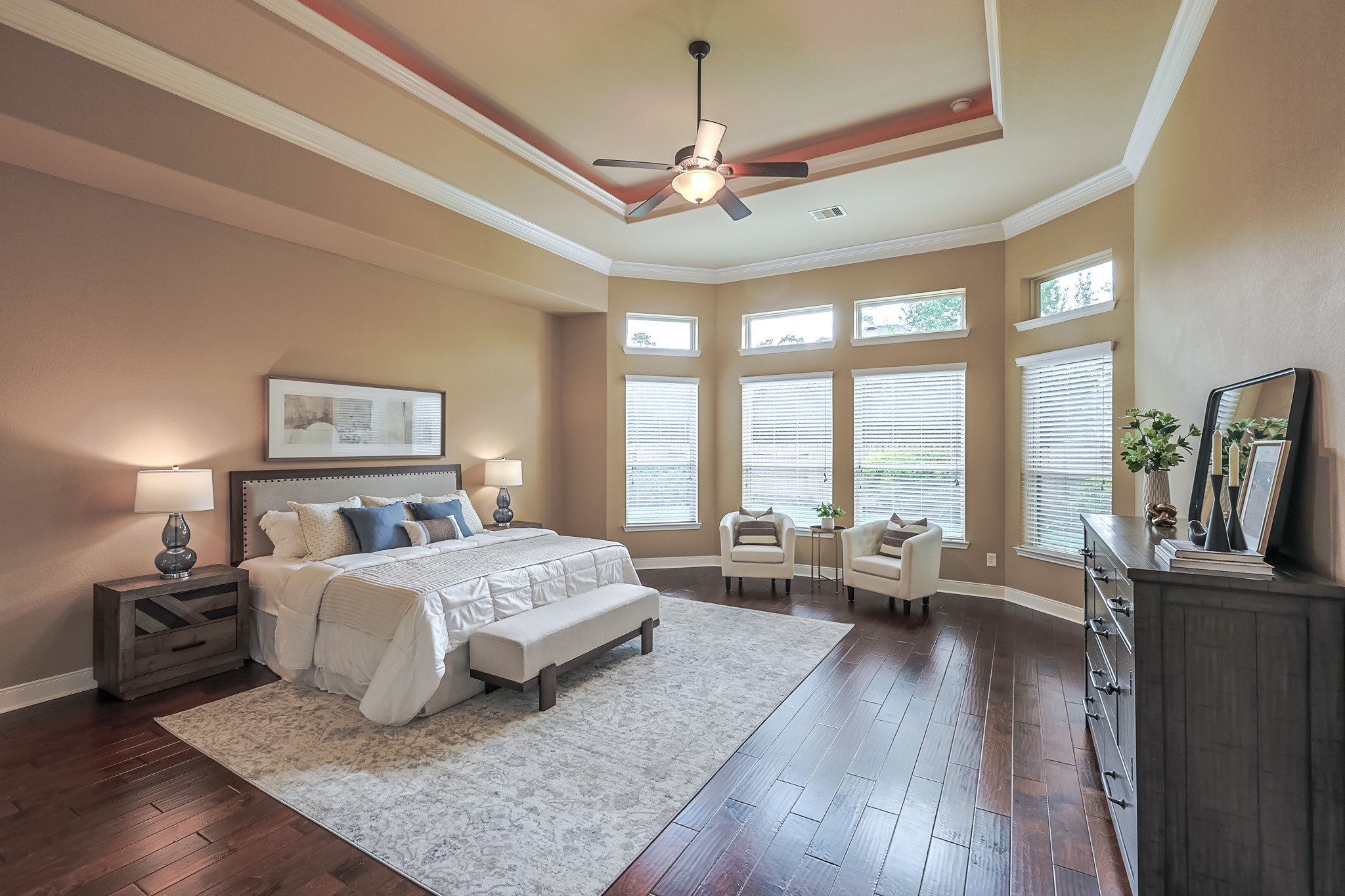 515 Mill Creek Road Pinehurst, TX 77362 - Photo 24 of 48 This spacious bedroom features a tray ceiling with recessed lighting and a ceiling fan. Large windows provide ample natural light, complementing the warm color palette. Elegant hardwood floors add to the inviting atmosphere.