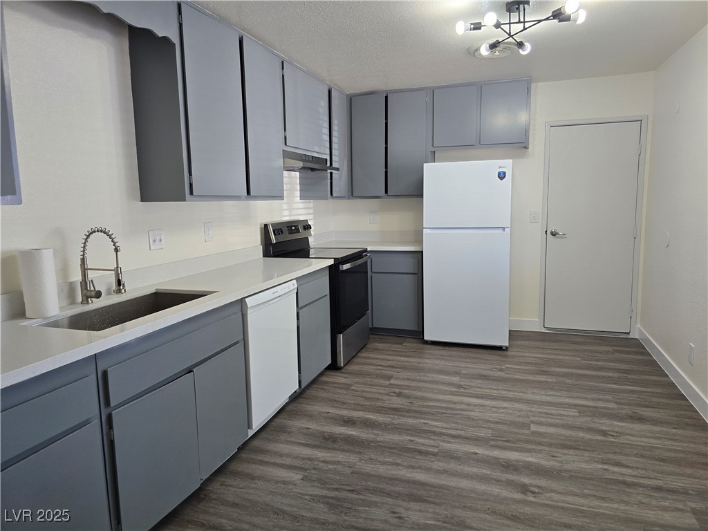 Kitchen with gray cabinetry, white appliances, dark wood-style floors, and a textured ceiling