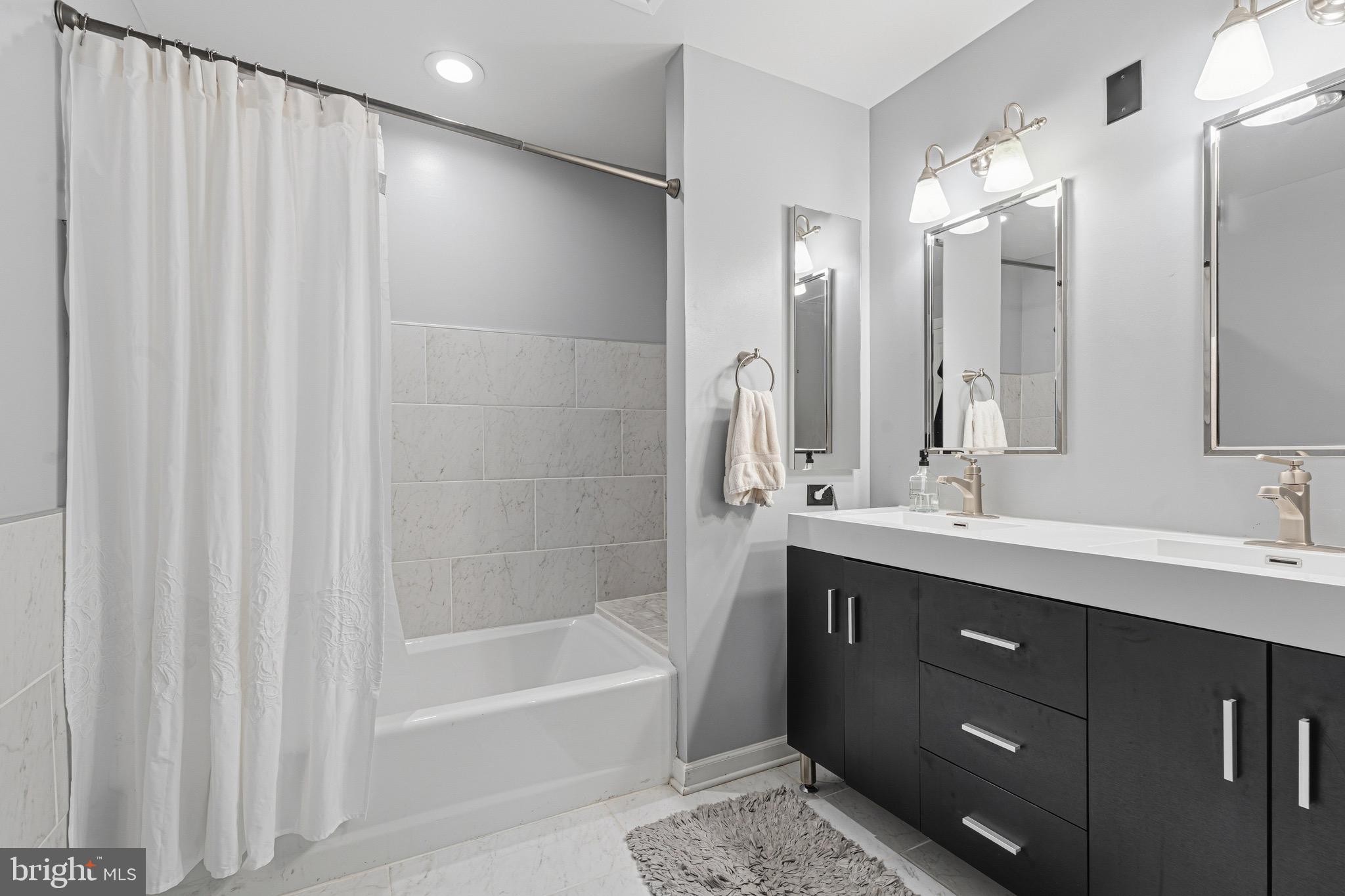 10 East Lee Street, Unit 808 Baltimore, MD 21202 - Photo 23 of 32 a bathroom with a double vanity sink a mirror and a bathtub