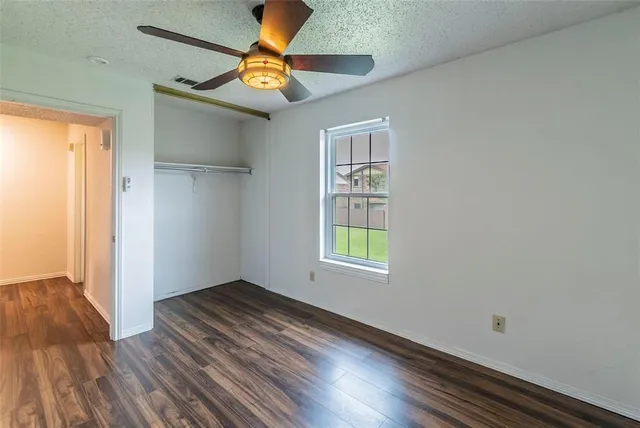 an empty room with wooden floor fan and windows