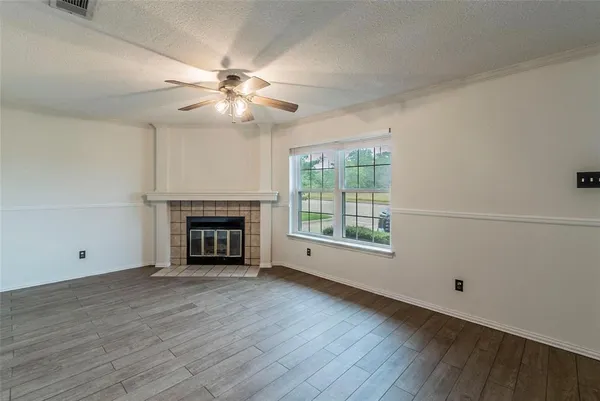 a view of an empty room with wooden floor fireplace and a window