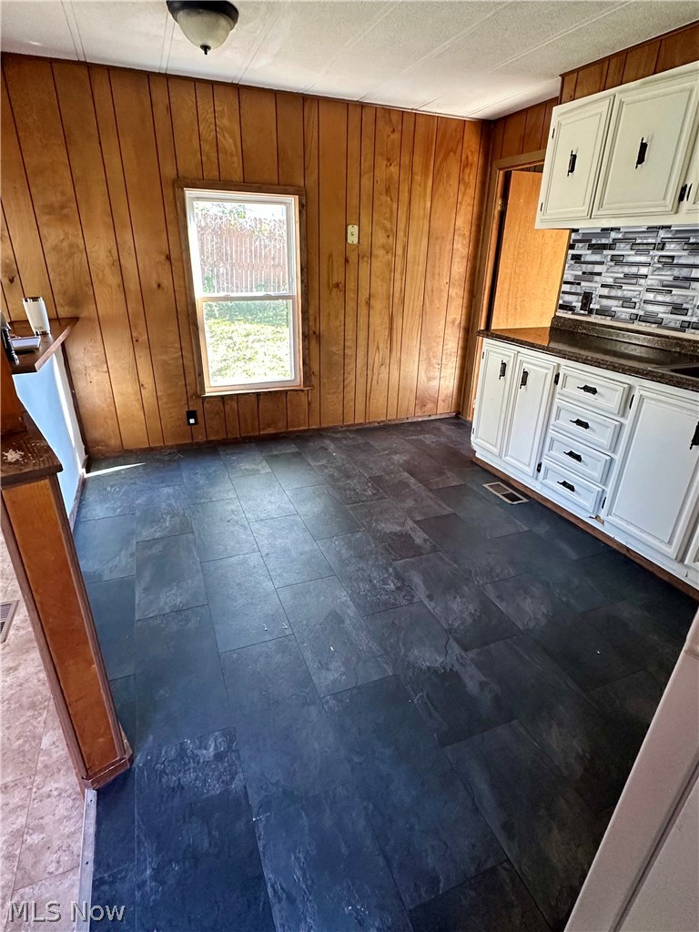 7443 Spillway Road Lisbon, OH 44432 - Photo 8 of 19 Kitchen featuring backsplash, dark tile flooring, wood walls, and white cabinetry