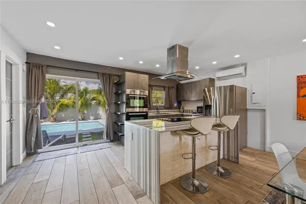 a kitchen with stainless steel appliances kitchen island granite countertop a stove a refrigerator a sink a dining table and chairs with wooden floor