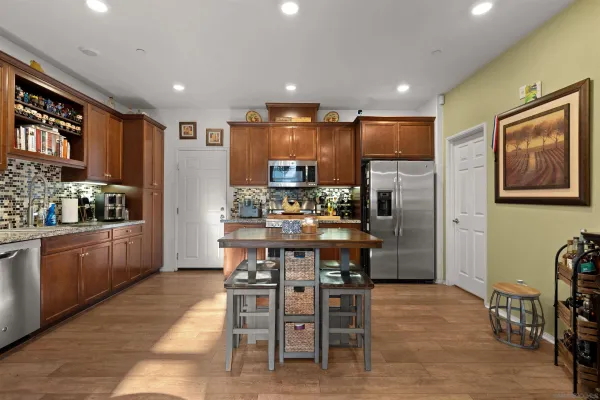a kitchen with stainless steel appliances kitchen island granite countertop a refrigerator a stove a sink a dining table and chairs with wooden floor