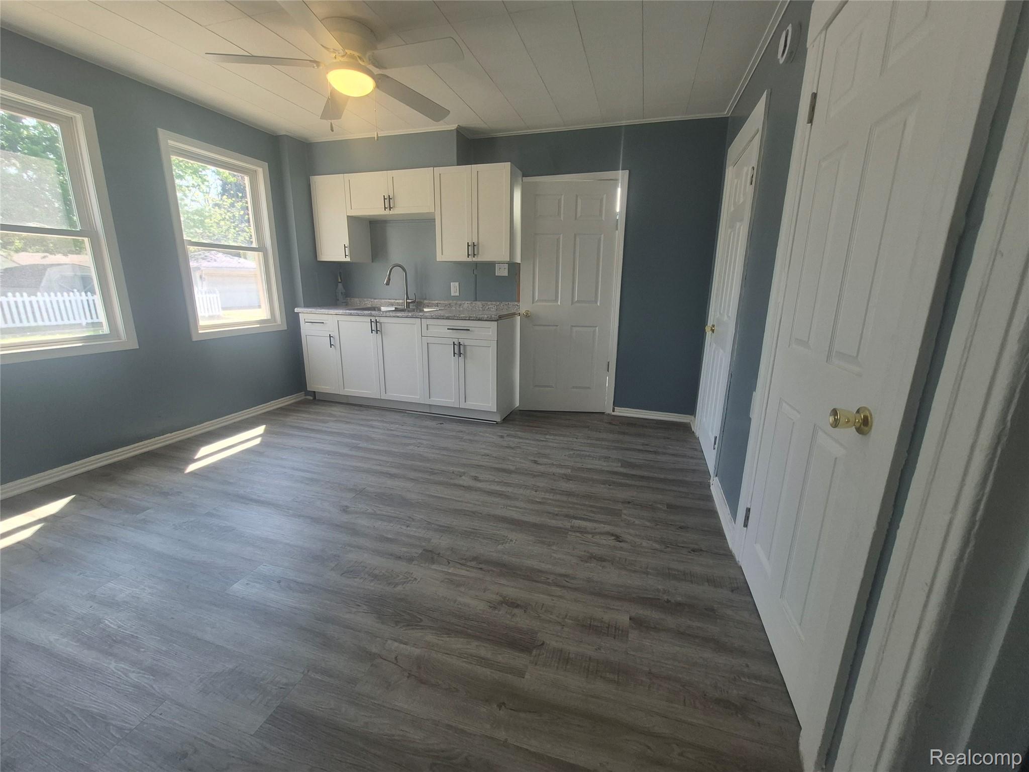 16758 Frazho Road Roseville, MI 48066 - Photo 12 of 53 Wood-finish flooring, white cabinetry with dark hardware, a stainless steel sink with a gooseneck faucet, two windows, and a ceiling fan with integrated lighting
