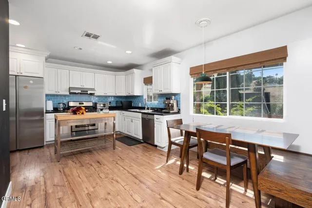 a kitchen with stainless steel appliances granite countertop a stove a refrigerator a sink a dining table and chairs with wooden floor