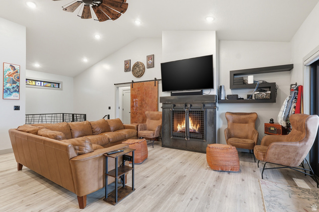 175 North 100 West Providence, UT 84332 - Photo 6 of 45 Great room featuring ceiling fan, light wood-style flooring, a warm lit fireplace, lofted ceiling, and a barn door