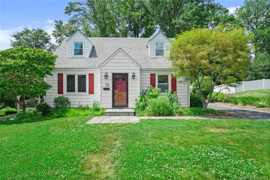 a view of a white house with a big yard plants and large trees