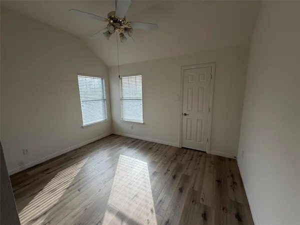 an empty room with wooden floor chandelier fan and windows