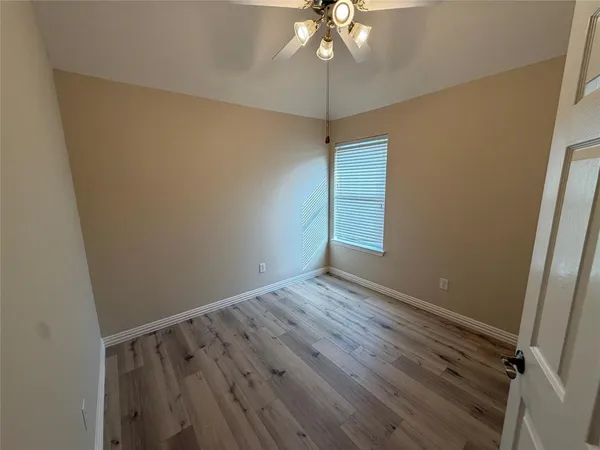 an empty room with wooden floor fan and windows