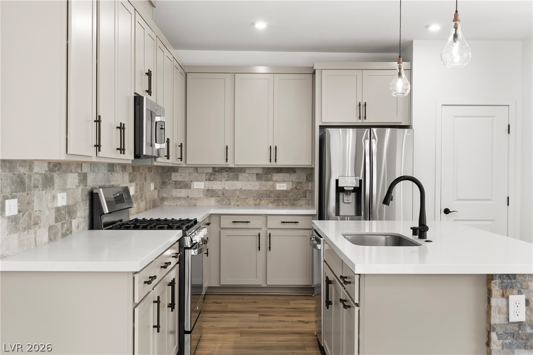 633 Infinity Rdg Street Las Vegas, NV 89138 - Photo 5 of 30 Kitchen featuring stainless steel appliances, gray cabinetry, an island with sink, decorative backsplash, and hanging light fixtures