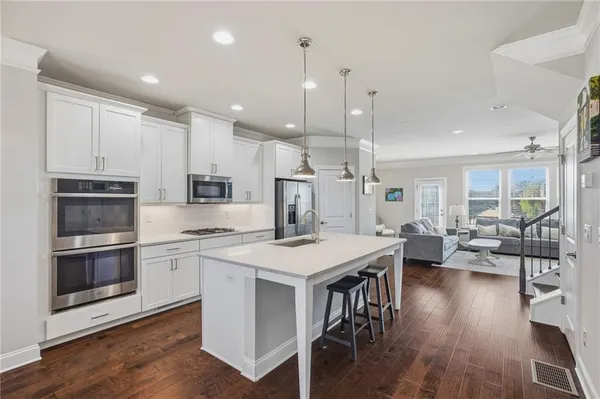 a kitchen with stainless steel appliances granite countertop a stove top oven a refrigerator a sink and white cabinets with wooden floor