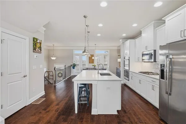 a kitchen with stainless steel appliances kitchen island granite countertop a stove a sink a refrigerator and white cabinets with wooden floor