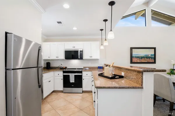 a kitchen with granite countertop a refrigerator a stove a sink and white cabinets