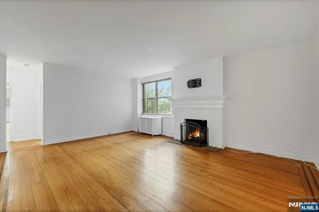 a view of an empty room with wooden floor fireplace and a window