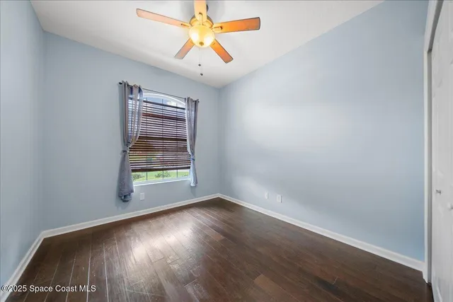 an empty room with wooden floor chandelier fan and windows