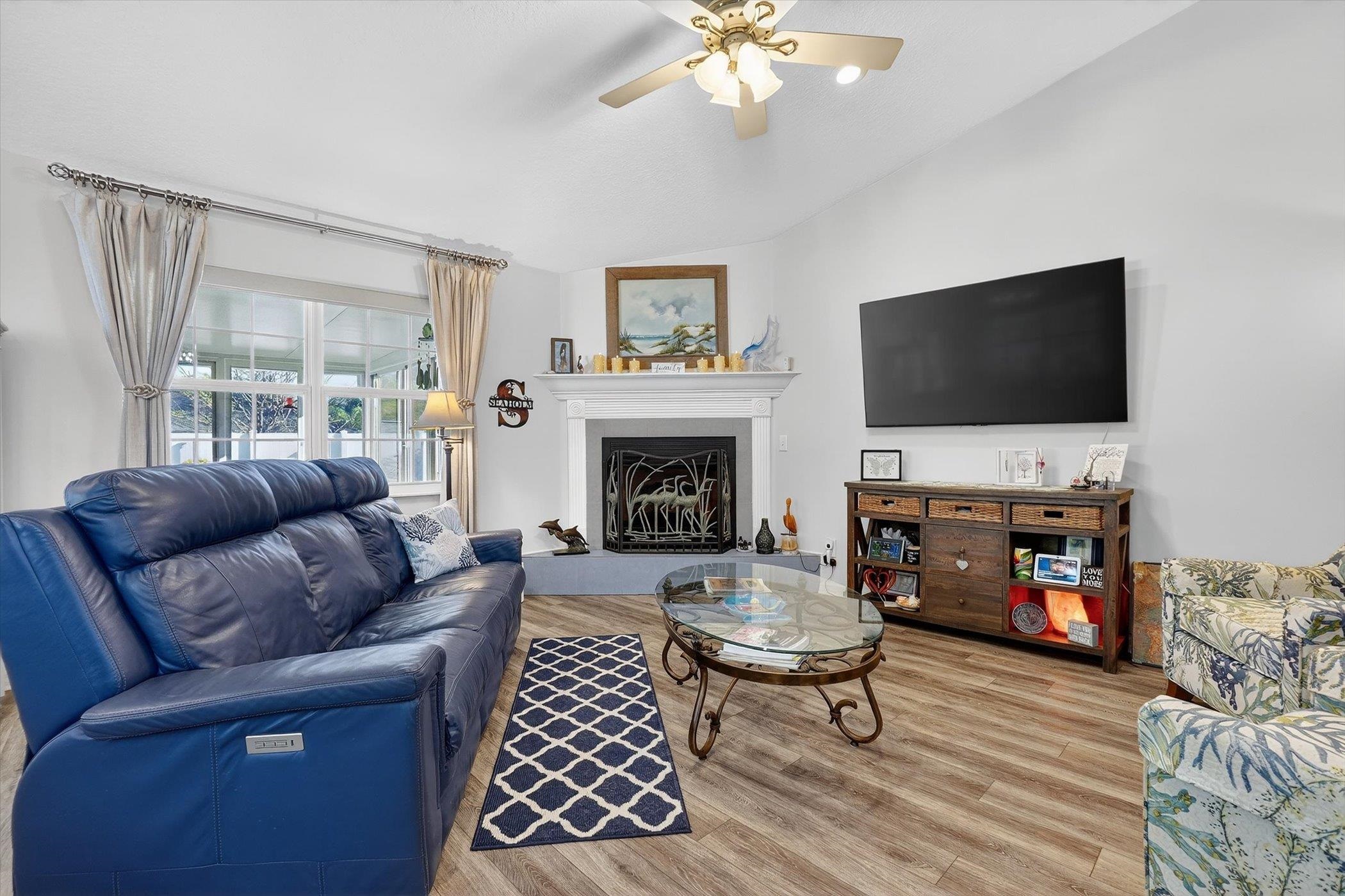 Living area featuring ceiling fan, light wood finished floors, vaulted ceiling, and a fireplace with raised hearth