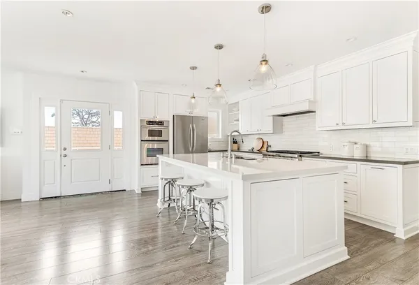 a kitchen with stainless steel appliances granite countertop a refrigerator a stove a sink and white cabinets with wooden floor