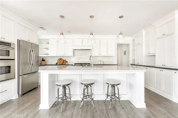 a kitchen with stainless steel appliances granite countertop a refrigerator a stove a sink and white cabinets with wooden floor