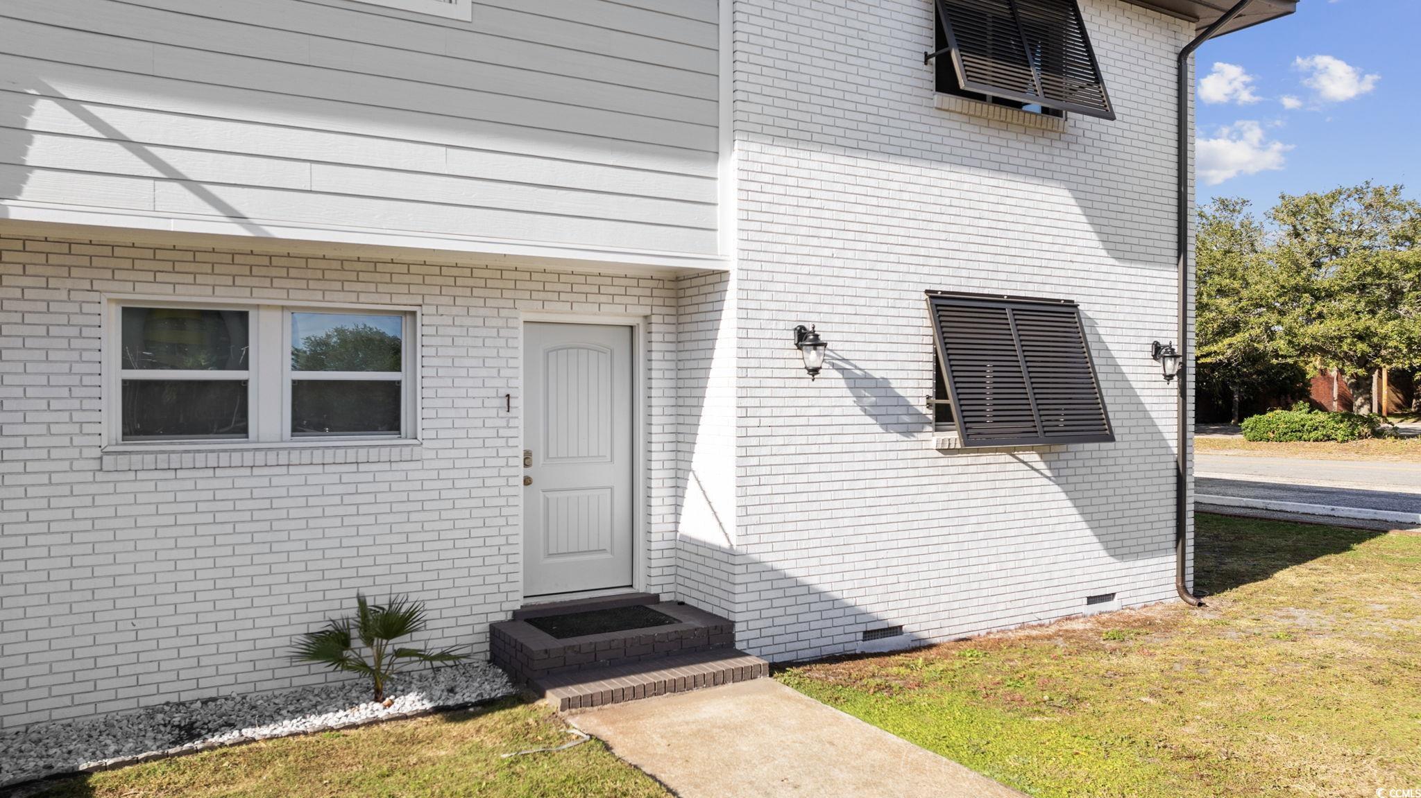 409 17th Avenue North, Unit 1 Myrtle Beach, SC 29577 - Photo 2 of 26 View of exterior entry featuring crawl space, a yard, and brick siding