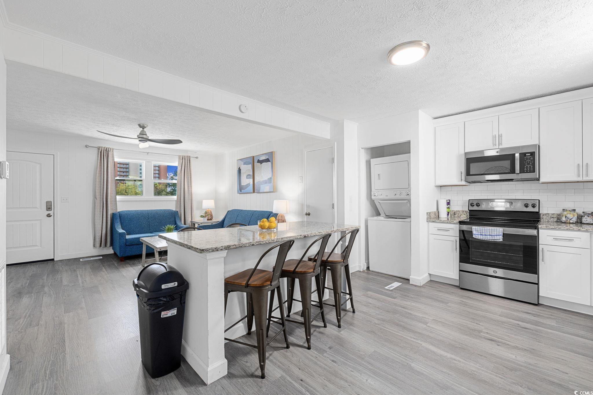 409 17th Avenue North, Unit 1 Myrtle Beach, SC 29577 - Photo 6 of 26 Kitchen with stainless steel appliances, light stone counters, backsplash, a textured ceiling, and light wood-style floors