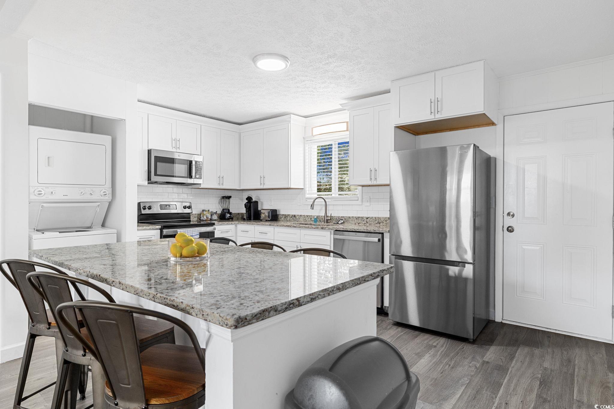 409 17th Avenue North, Unit 1 Myrtle Beach, SC 29577 - Photo 7 of 26 Kitchen featuring light stone counters, stainless steel appliances, dark wood-style floors, a textured ceiling, and white cabinetry