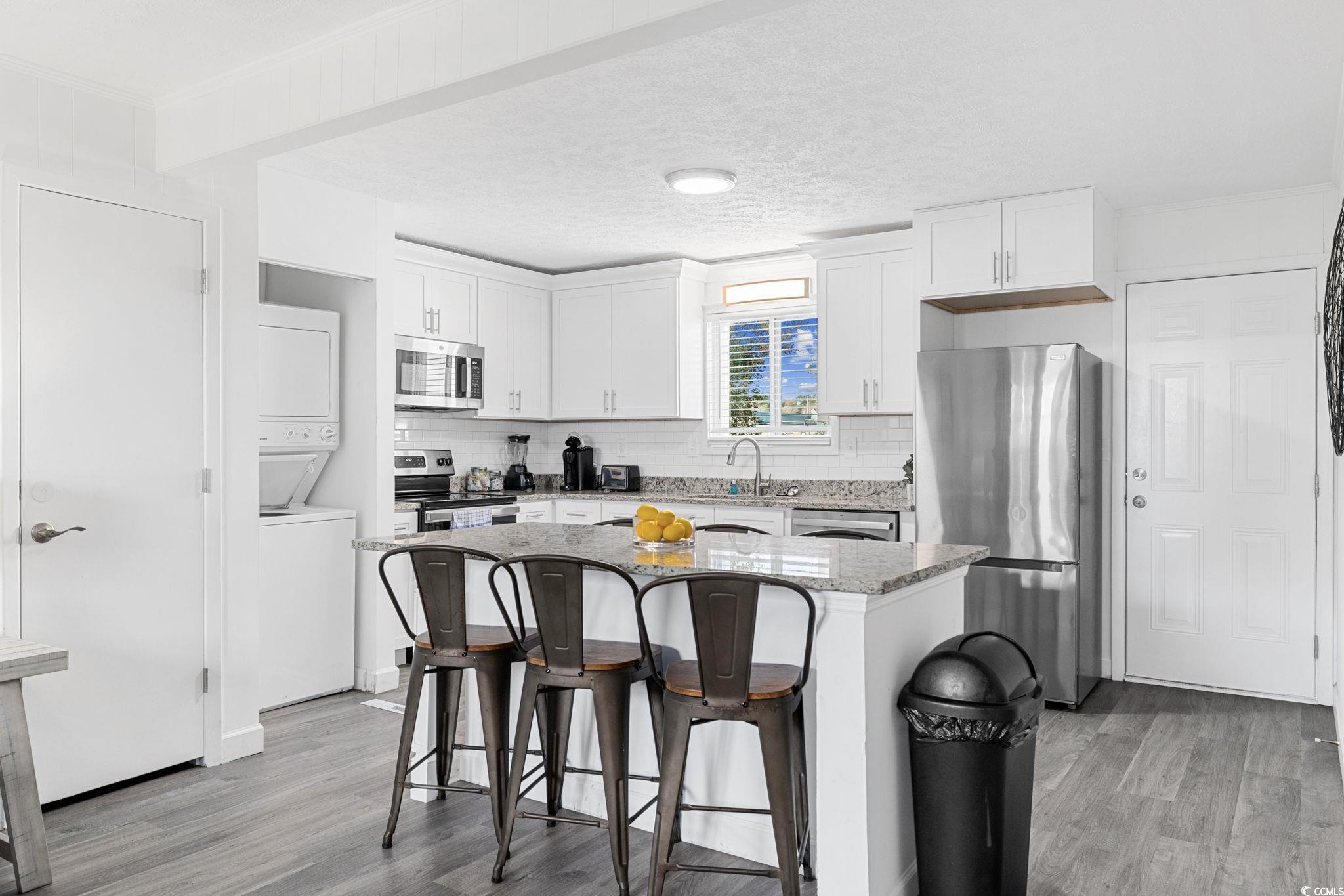 409 17th Avenue North, Unit 1 Myrtle Beach, SC 29577 - Photo 8 of 26 Kitchen featuring a breakfast bar area, appliances with stainless steel finishes, light stone countertops, light wood finished floors, and a textured ceiling