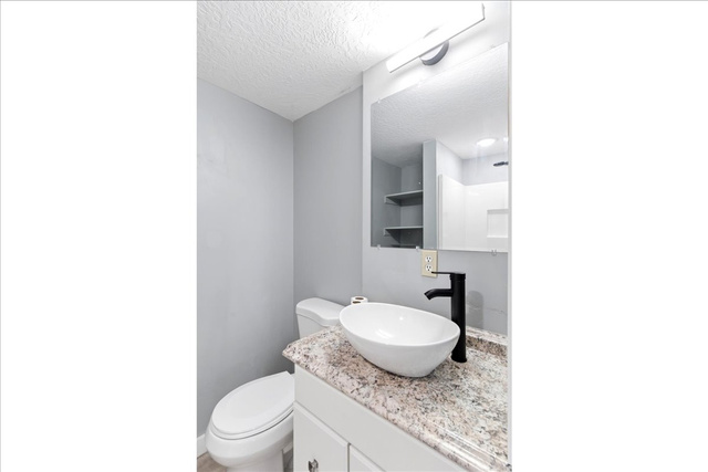1613 Sunset Road Lake Point, UT 84074 - Photo 23 of 33 Modern bathroom featuring a vessel sink, dark-finish faucet, granite-style countertop, and vanity mirror with integrated lighting