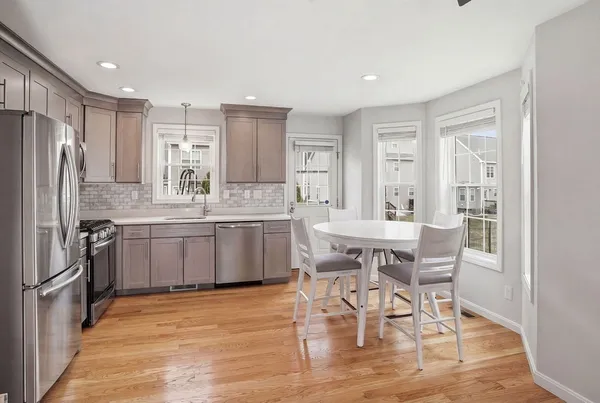 a kitchen with stainless steel appliances kitchen island granite countertop a dining table chairs and a refrigerator