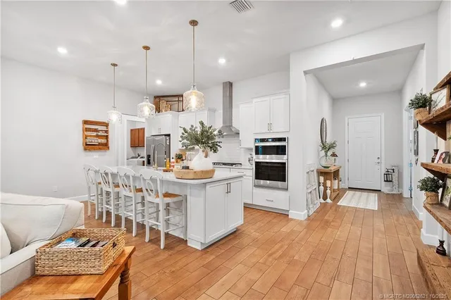 a kitchen with stainless steel appliances kitchen island granite countertop a stove a sink a refrigerator and chairs with wooden floor