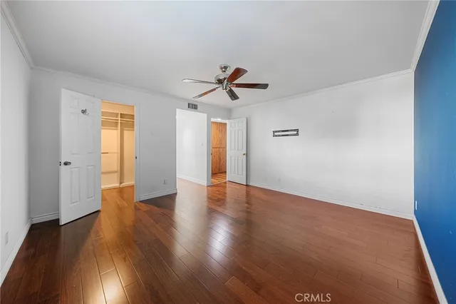 a view of an empty room with wooden floor and a ceiling fan