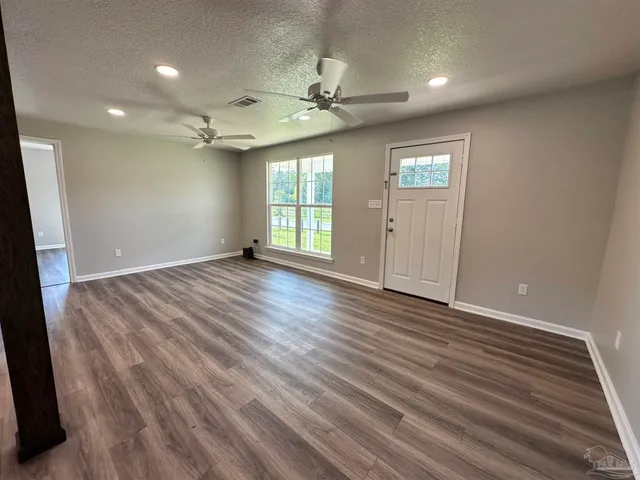 an empty room with wooden floor fan and windows