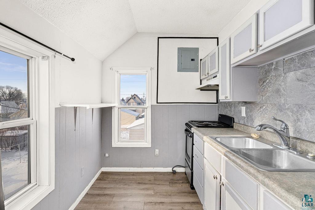 605 Weeks Avenue Superior, WI 54880 - Photo 3 of 21 Kitchen featuring freestanding range oven, vaulted ceiling, light countertops, light wood-style flooring, and electric panel