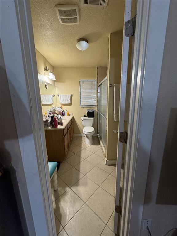 636 East Kempner Street Mabank, TX 75147 - Photo 27 of 28 Bathroom featuring a single vanity with wood-finish cabinetry and a light-toned countertop, a toilet, a shower enclosure with glass doors, and diagonal tile flooring