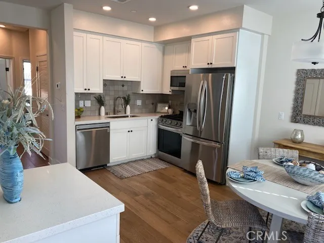 a kitchen with stainless steel appliances granite countertop a refrigerator a stove a sink a dining table and chairs with wooden floor