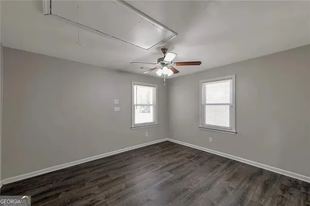 an empty room with wooden floor windows and fan