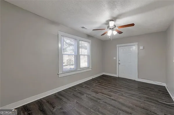 an empty room with wooden floor ceiling fan and windows
