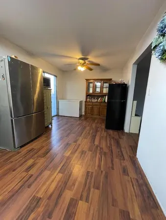 a view of a refrigerator in kitchen and an empty room with wooden floor