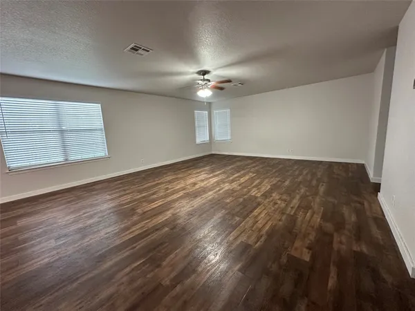 an empty room with wooden floor ceiling fan and windows