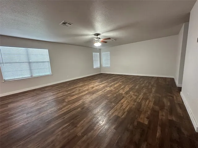 an empty room with wooden floor ceiling fan and windows