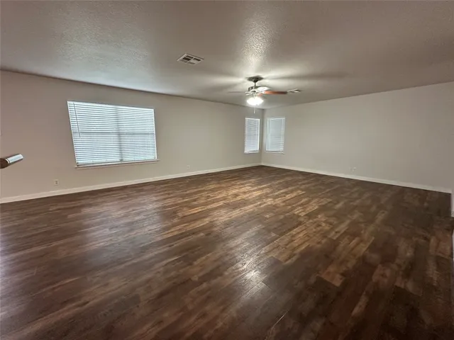an empty room with wooden floor ceiling fan and windows