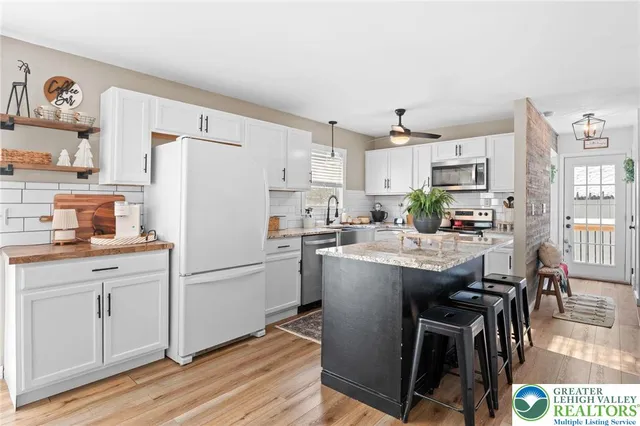 a kitchen with stainless steel appliances granite countertop a refrigerator a sink dishwasher a stove and white countertops with wooden floor